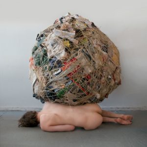 nude woman, prone, burdened by a sphere of garbage